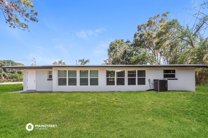 the front of a white house with a lawn and trees