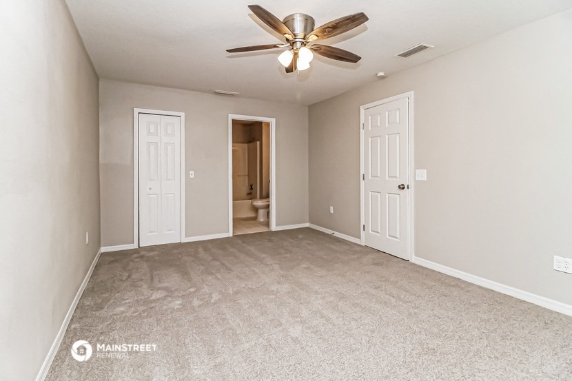 an empty living room with a ceiling fan and a door to a bathroom