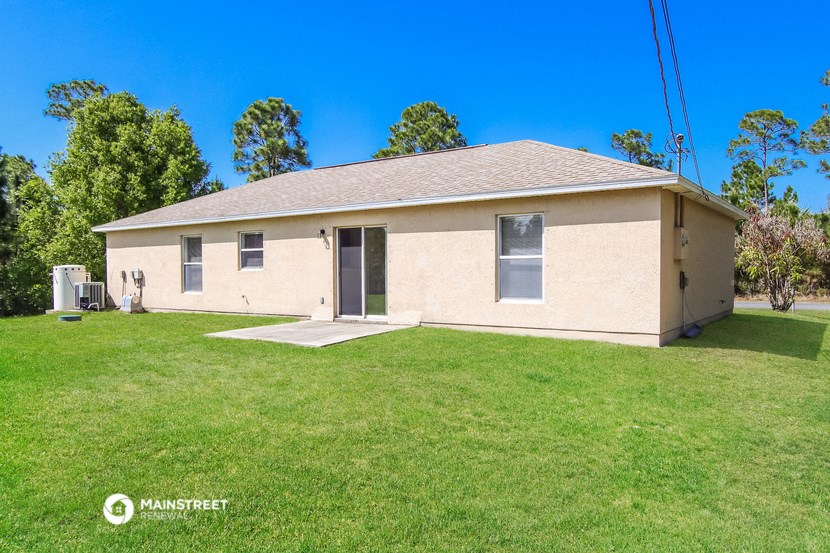 a small tan brick home with a grassy yard and trees