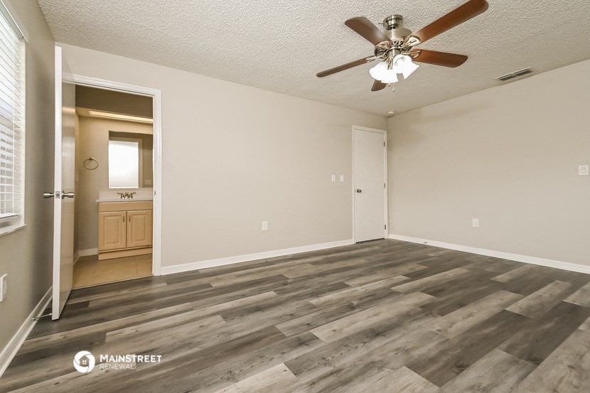 the spacious living room with wood flooring and a ceiling fan