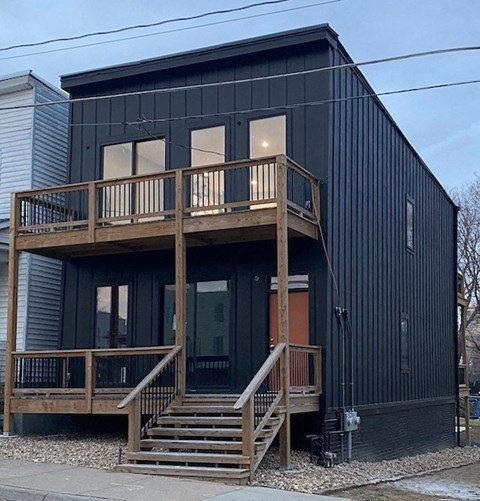 A black house with a wooden deck and stairs.