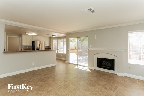 A spacious living room with a fireplace and a kitchen area in the background.