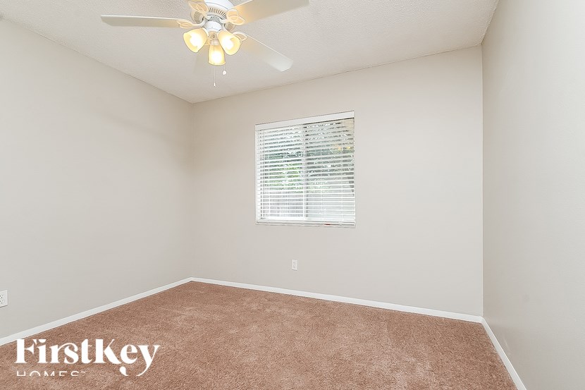 A room with a carpeted floor, a ceiling fan, and a window with blinds.