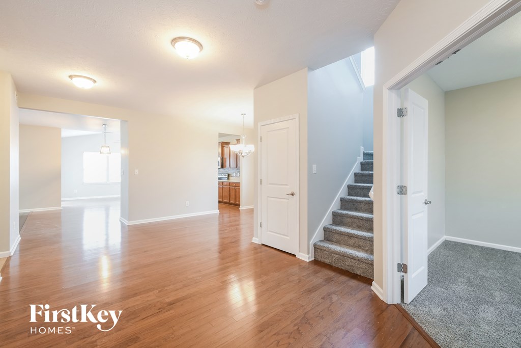 A spacious room with wooden floors and a staircase leading to another room.
