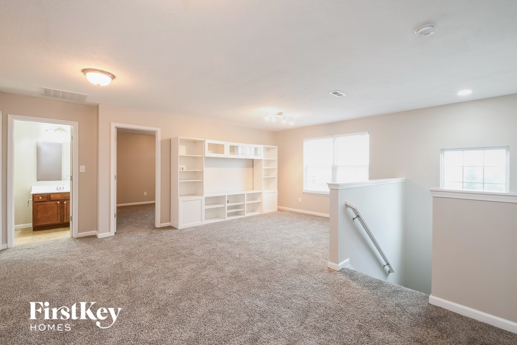 A spacious room with a carpeted floor and a staircase on the right side.