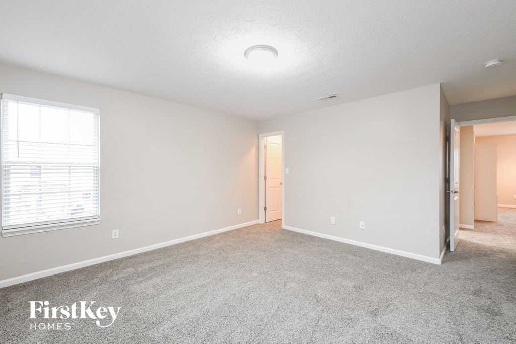 A spacious empty room with a carpeted floor and a door in the background.