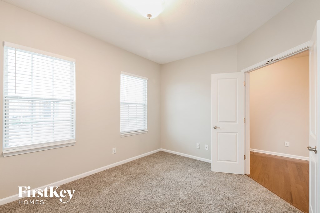 A room with a carpeted floor, a door, and a window with blinds.