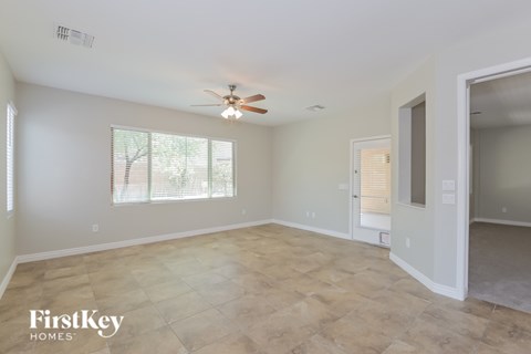 A spacious room with a ceiling fan and light fixture, and a doorway leading to another room.