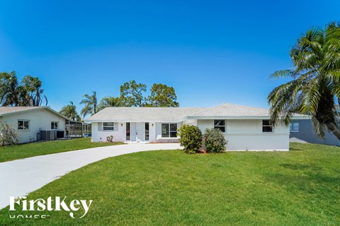 a white house with a green lawn and palm trees