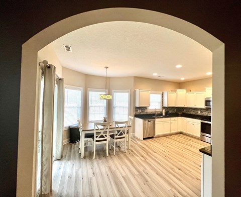 A kitchen with a dining table and chairs is visible through an archway.