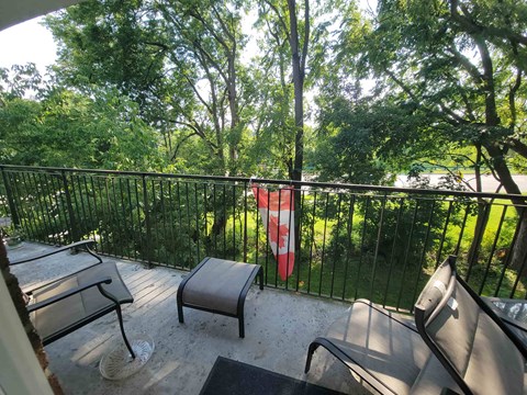 A balcony with a black railing, a bench, a table and a flag.