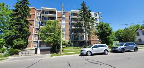 A silver car is parked on the street in front of a multi-story apartment building.