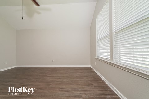 the bedroom of a home with a large window and wood flooring