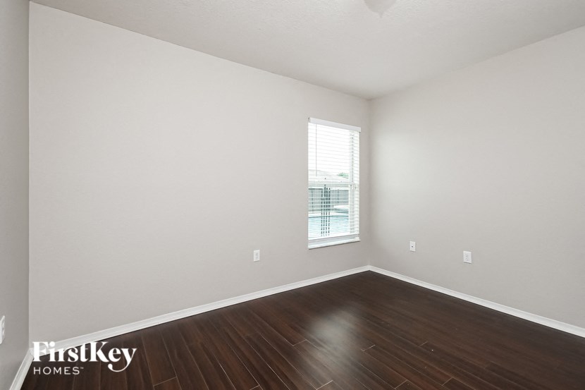 a bedroom with white walls and wood floors and a window