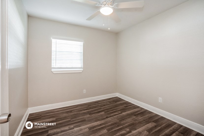 the spacious living room with hardwood flooring and a ceiling fan