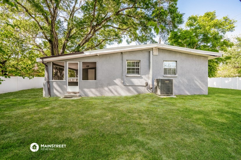a small gray house with a lawn and trees