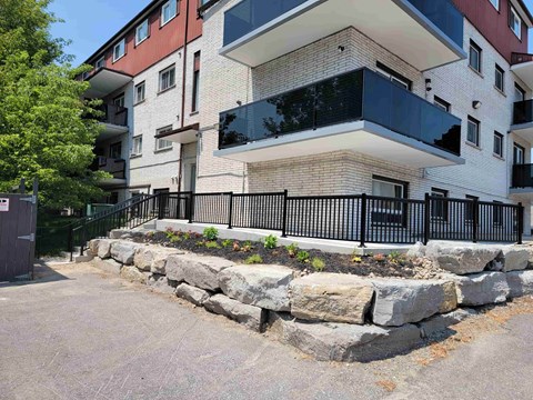 A modern multi-story building with balconies and a stone wall in front.