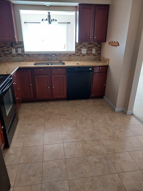 A kitchen with brown cabinets and a black dishwasher.