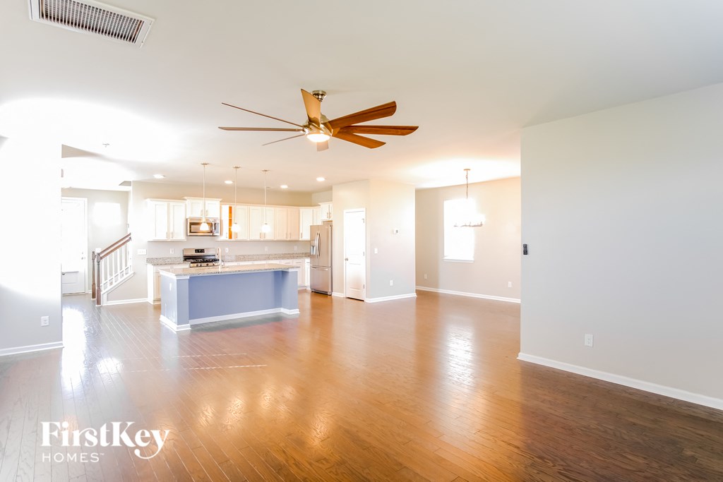 A spacious living room with a wooden floor and a ceiling fan.