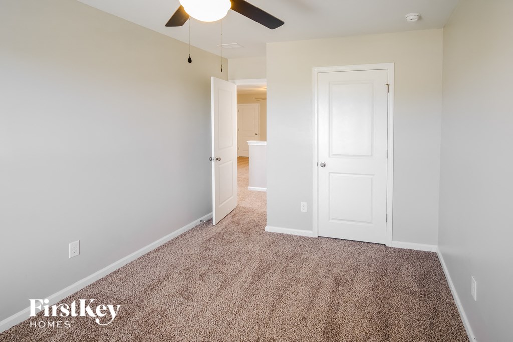 A carpeted room with a ceiling fan and two doors.
