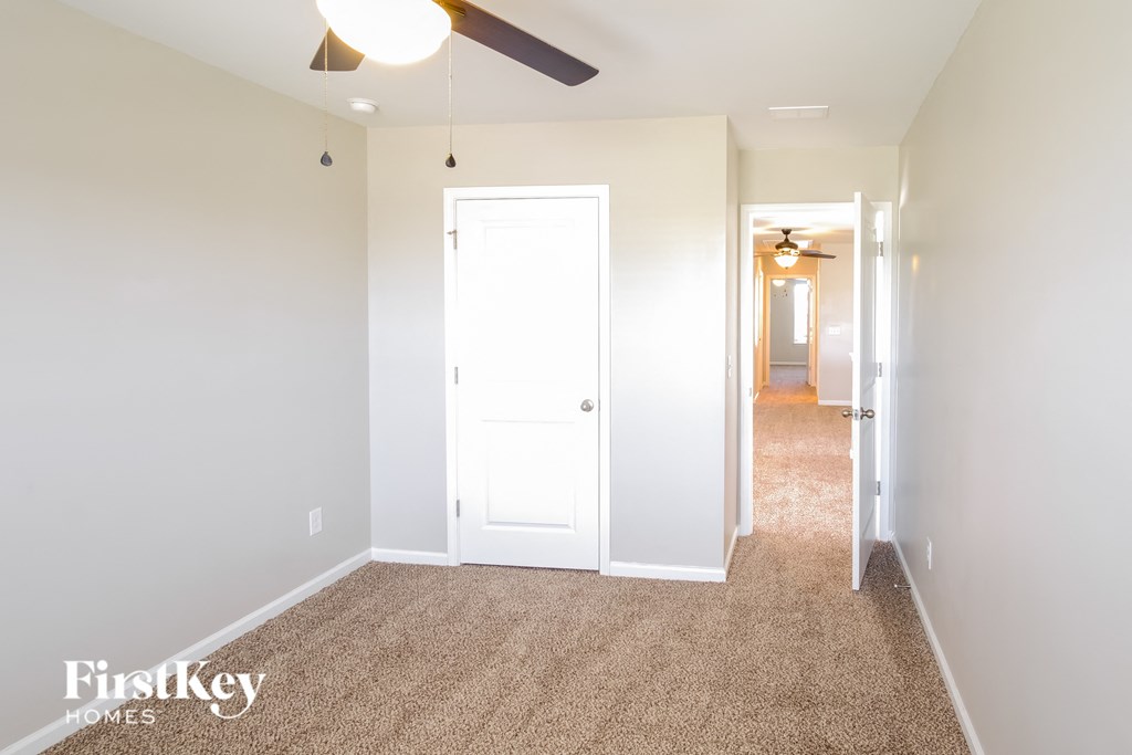 A carpeted hallway with a white door and a ceiling fan.