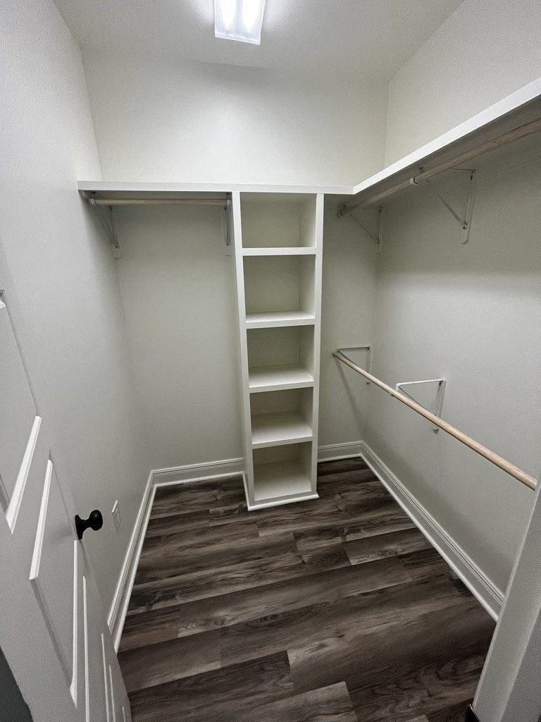a walk in closet with shelves and a wood floor