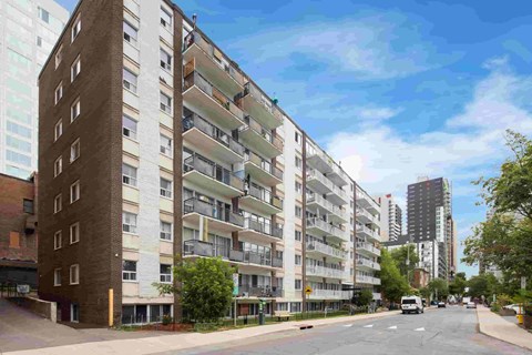 A street view of a residential area with apartment buildings on the left and a parked car on the road.