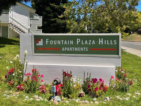 A sign for Fountain Plaza Hills Apartments is surrounded by flowers.