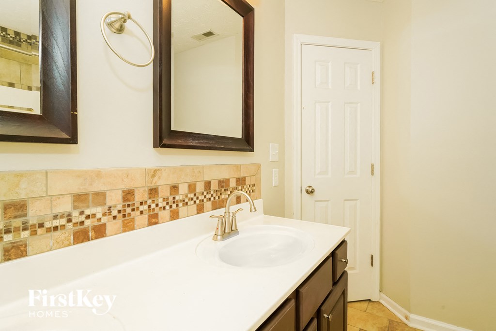 A bathroom with a sink, mirror and a door.