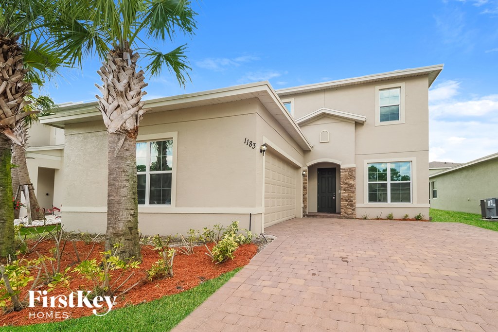 a beige house with a driveway and a palm tree