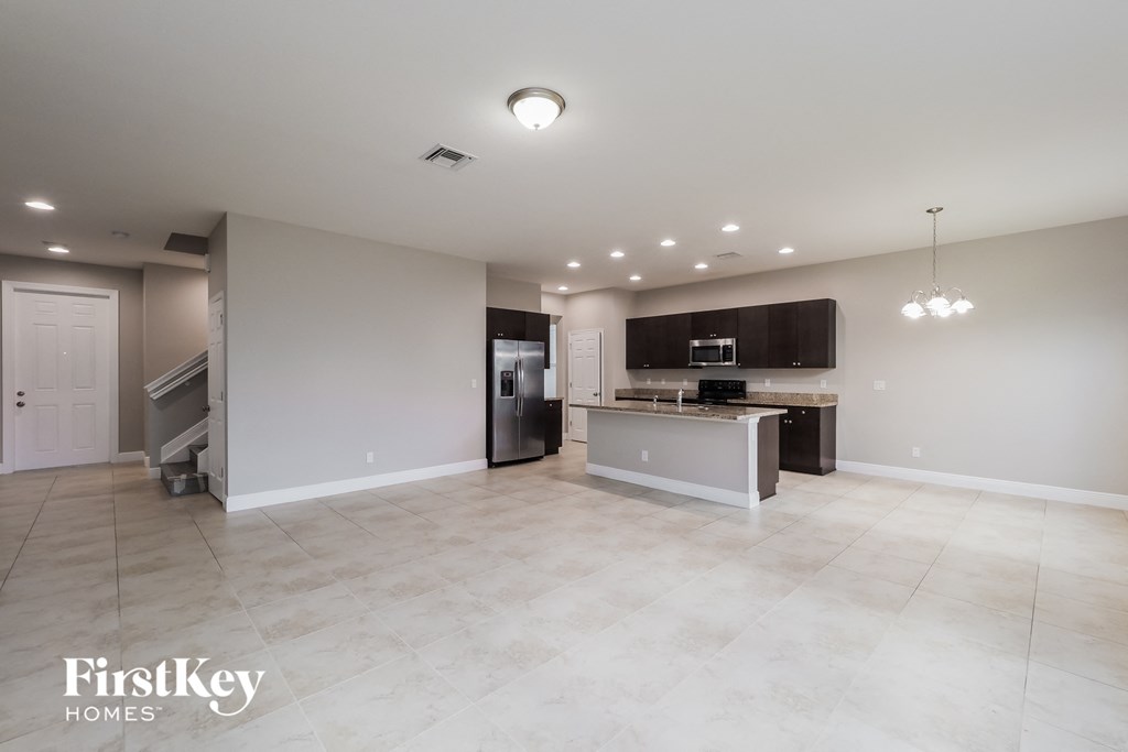 an open kitchen and living room with white tile flooring and stainless steel appliances