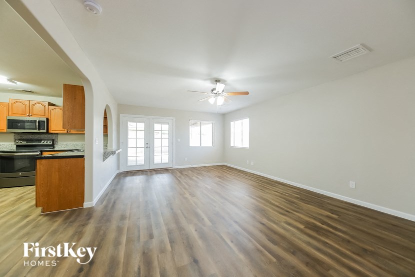 an empty living room and kitchen with wood flooring and a ceiling fan