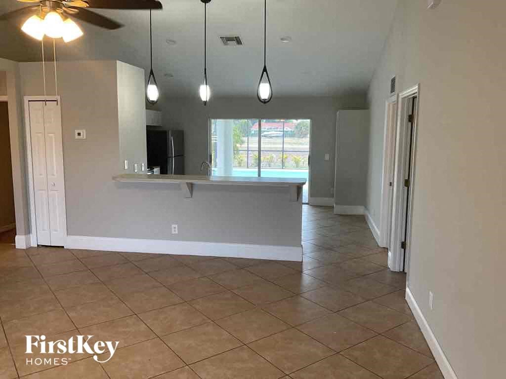an empty living room with a kitchen and a ceiling fan