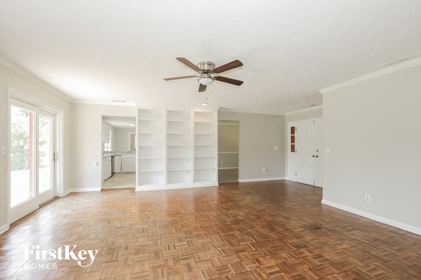 an empty living room with a ceiling fan and a book shelf