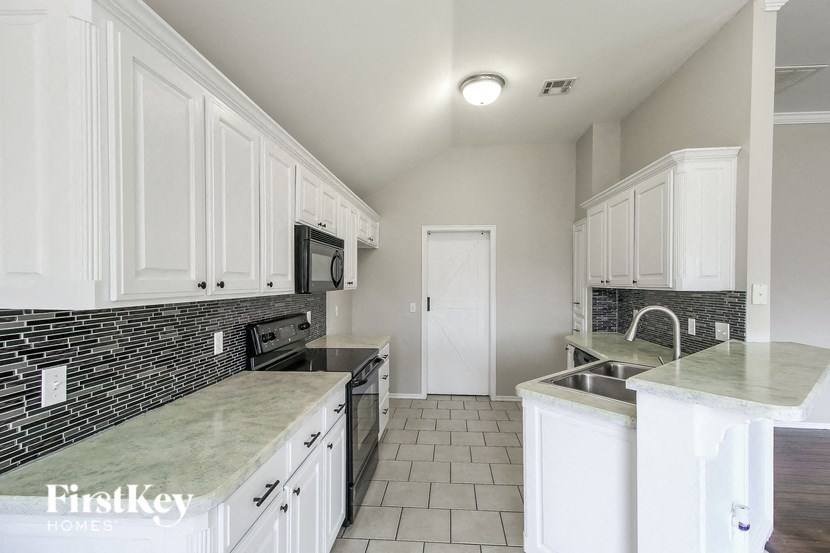 A kitchen with white cabinets and a black brick backsplash.