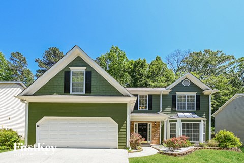 A green house with a white garage door and a brick chimney.