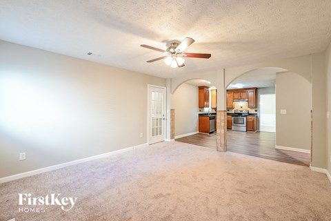 A spacious living room with a ceiling fan and a view of the kitchen.