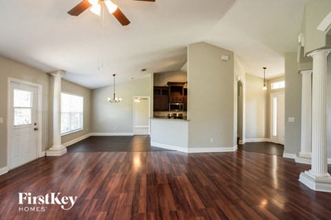 an empty living room with wood flooring and a kitchen
