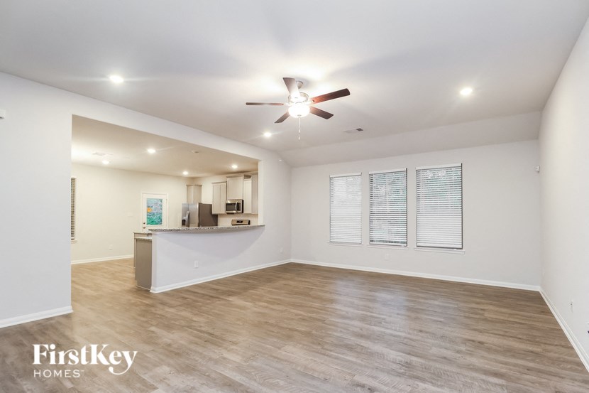 an empty living room with a ceiling fan and a kitchen