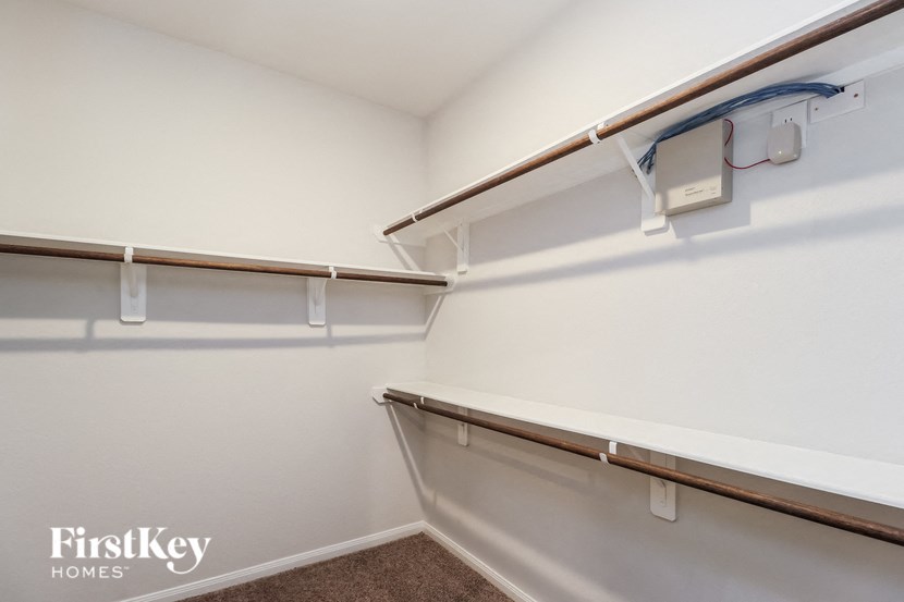 a walk in closet with white walls and white shelves and hooks on the wall
