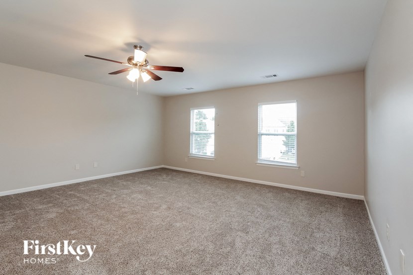 an empty living room with a ceiling fan and two windows