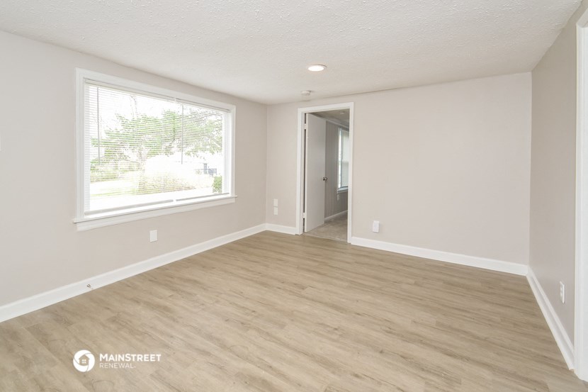 an empty living room with a large window and wood flooring