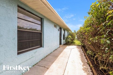 a side view of a blue house with a sidewalk and bushes