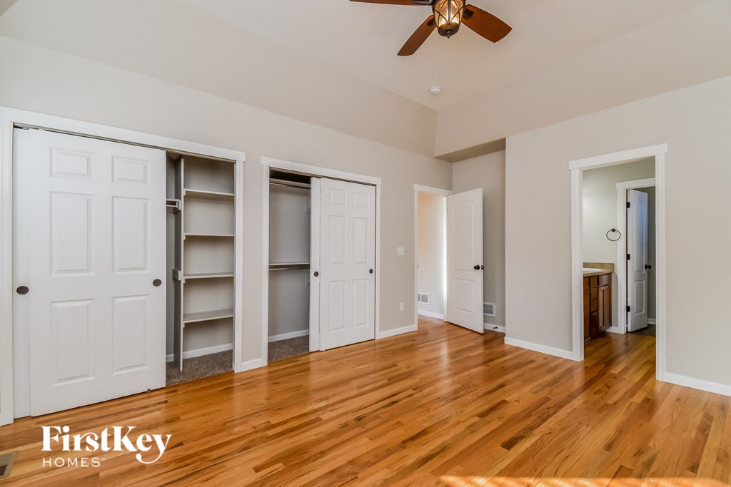 a bedroom with white closets and wood floors and a ceiling fan