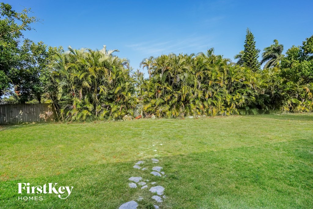 A lush green lawn with a pathway leading to a fence and trees.