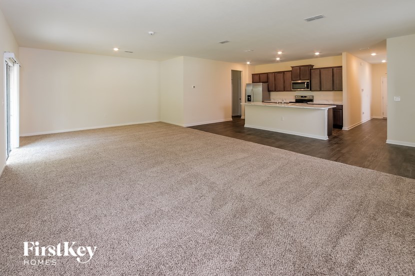 A spacious living room with a kitchen in the background.
