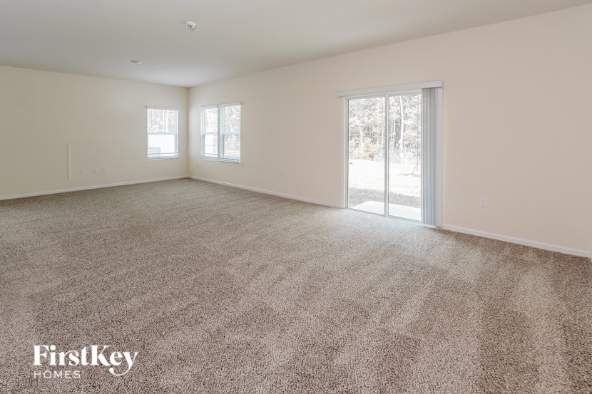 A spacious room with a carpeted floor and two windows.