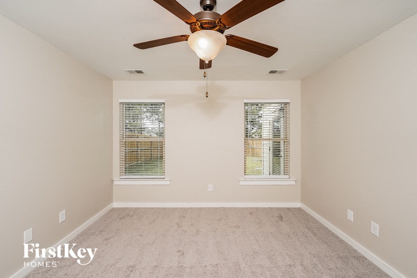A room with a ceiling fan and two windows.