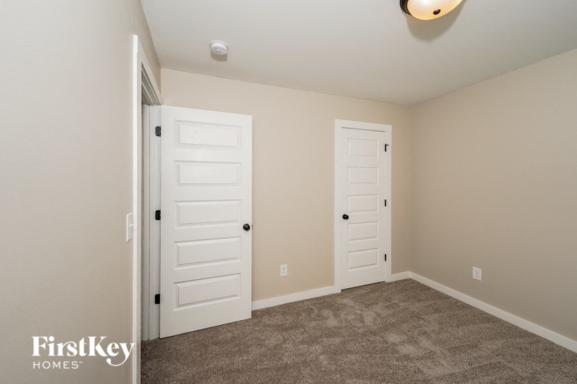 A carpeted room with two white doors and a light on the ceiling.