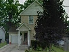 A small house with a porch and a tree in front.